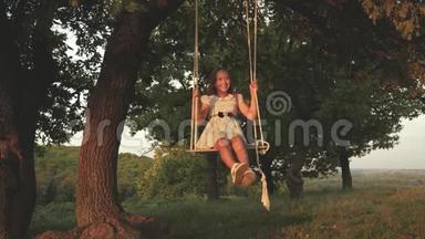 小女孩在阳光下的一棵树下<strong>荡秋千</strong>，和孩子们玩。 小孩骑着绳子在橡树枝上<strong>荡秋千</strong>